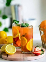 Two glasses of iced peach green tea lemonade sitting on a wooden tray with some lemon slices.