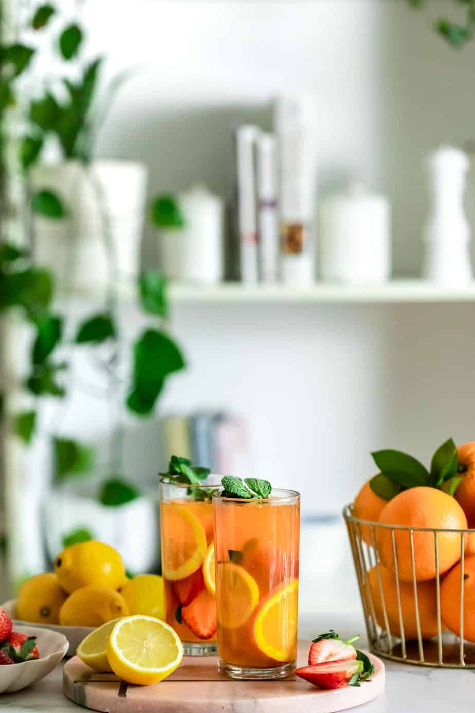 Two glasses of iced peach green tea lemonade sitting on a counter next to fresh fruit.