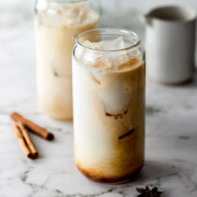 Two glasses of dirty chai latte over ice sitting on a marble counter.