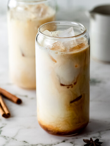 Two glasses of dirty chai latte over ice sitting on a marble counter.