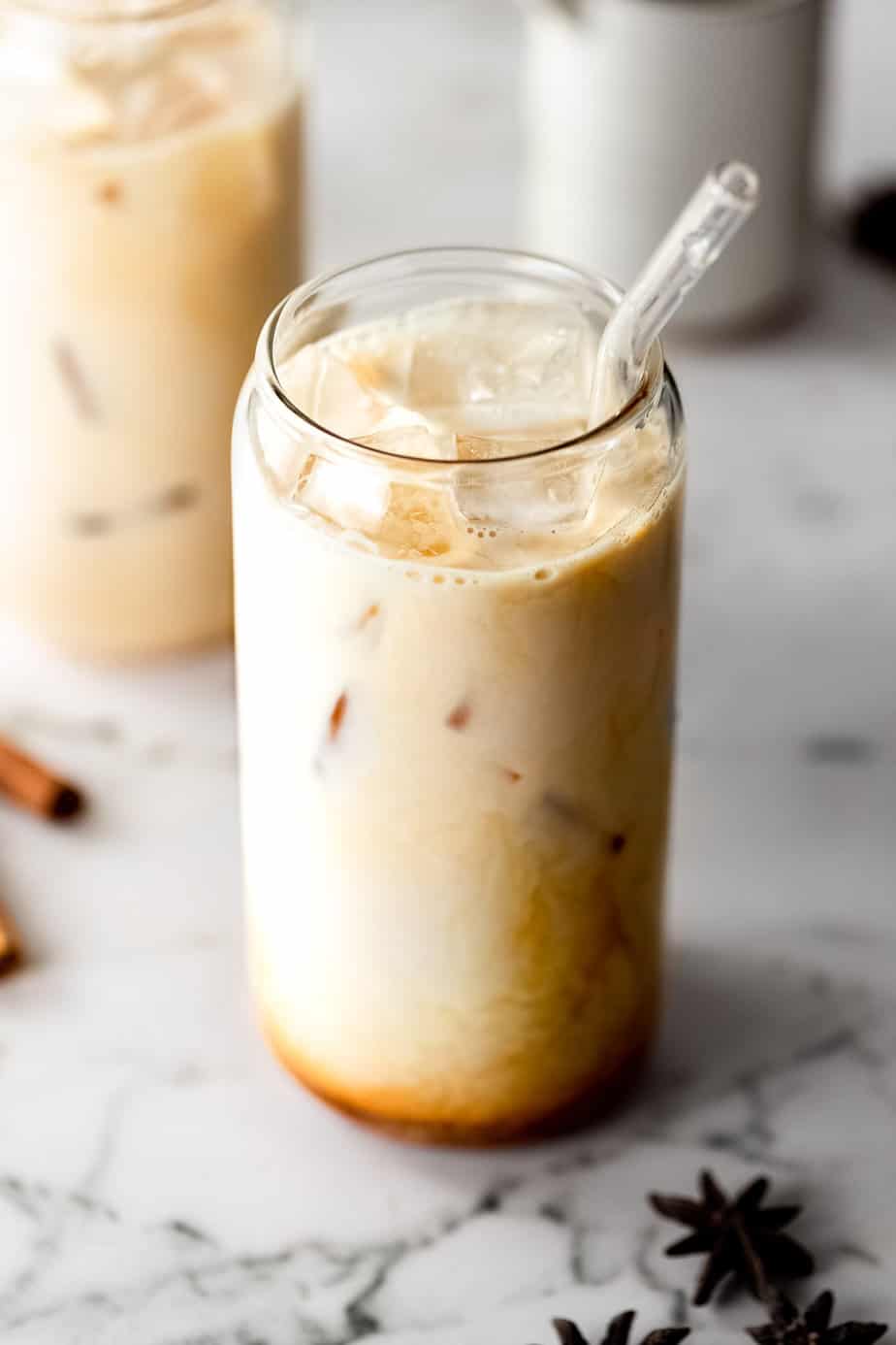 An iced dirty chai latte with ice cubes and whole dried spices sitting on a marble counter.