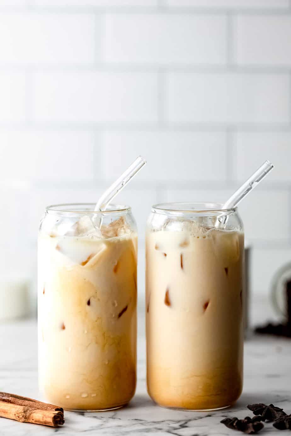 Two dirty chai lattes in serving glasses with glass straws.