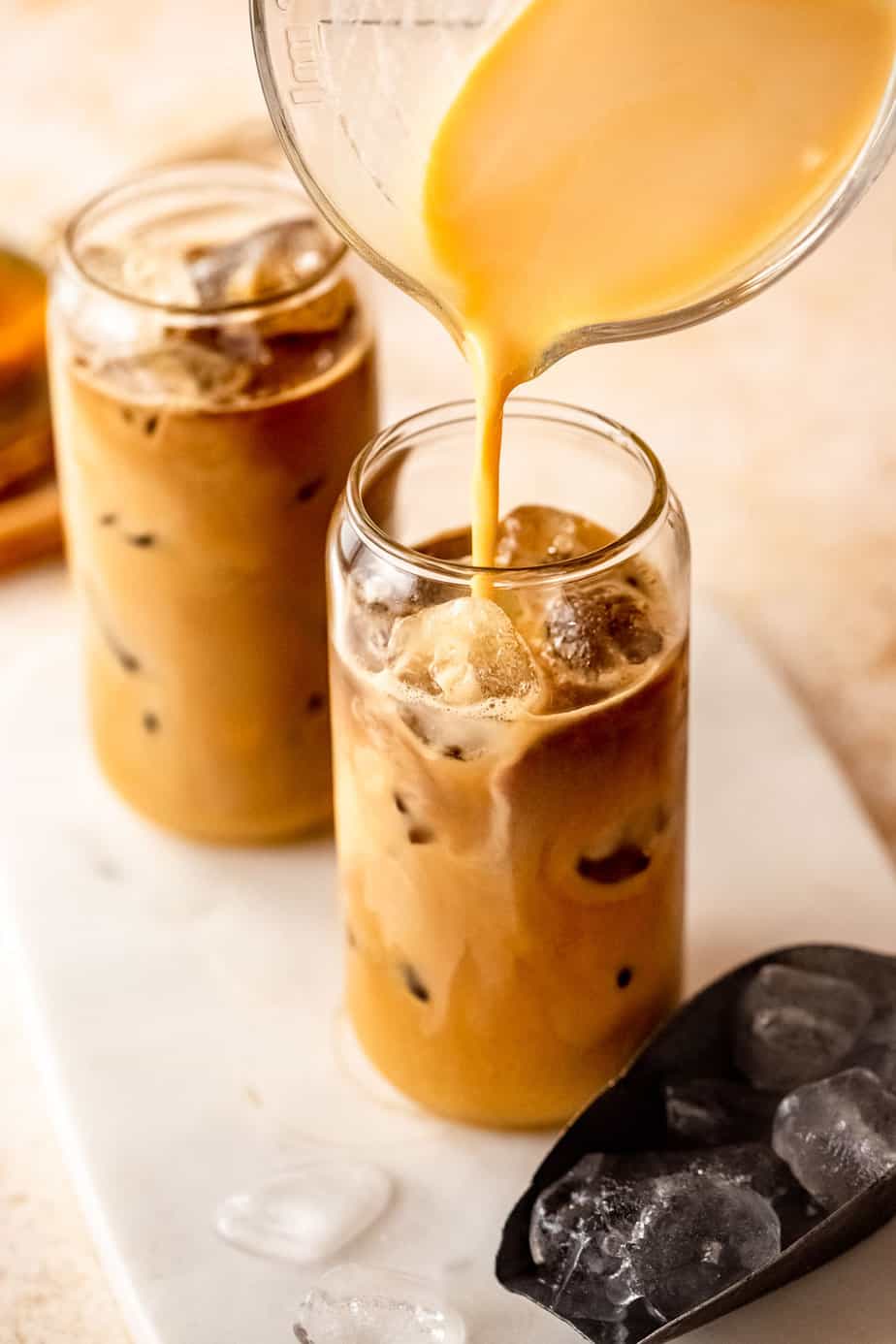 Pumpkin cream being poured over chai tea and ice cubes.