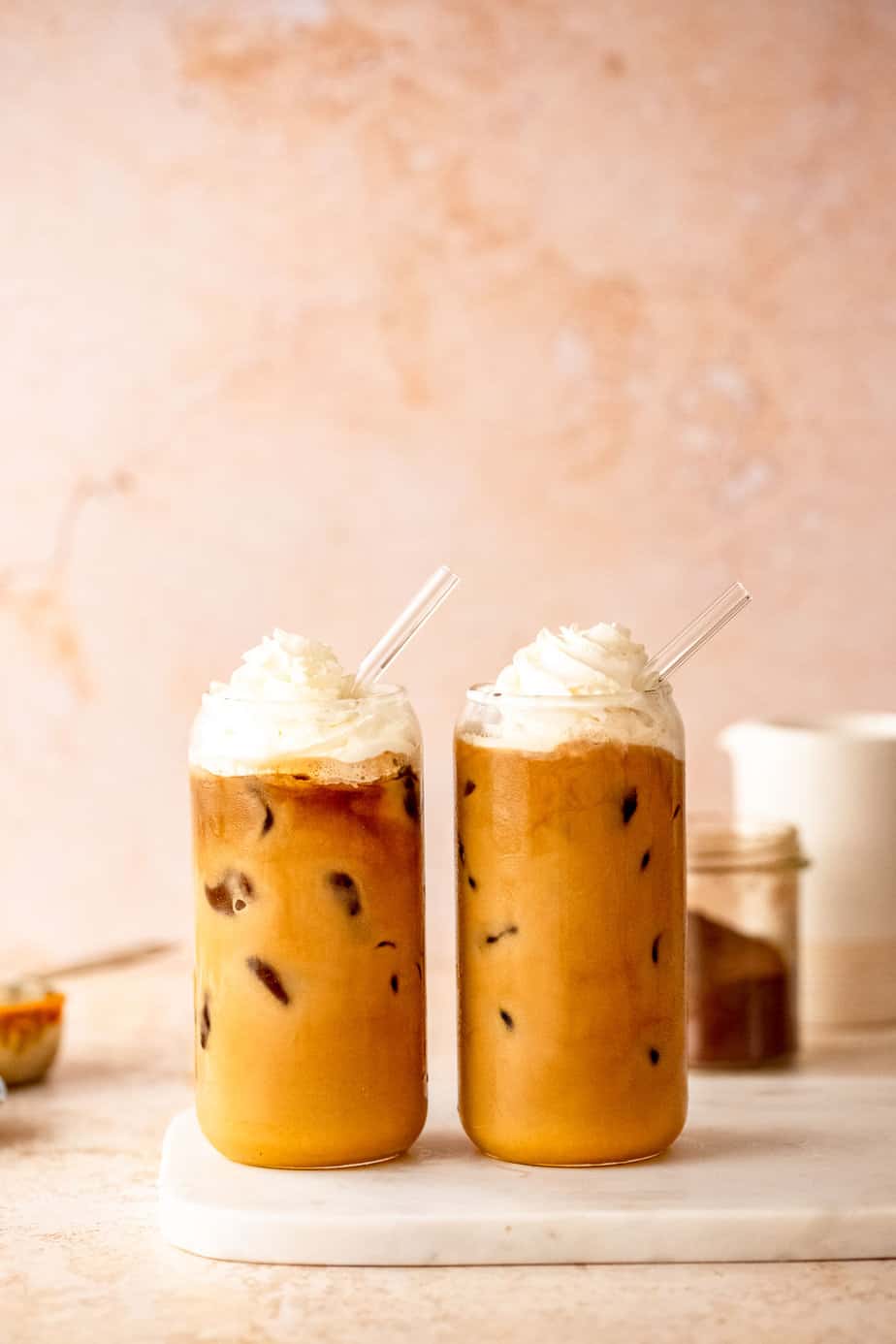 Two iced pumpkin chai lattes topped with whipped cream and glass straws.