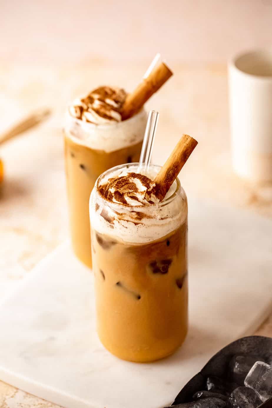 Two glasses of iced pumpkin chai latte topped with with whipped cream and cinnamon.