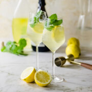 Two limoncello spritz cocktails in wine glasses sitting on a marble counter.