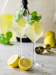 Two limoncello spritz cocktails in wine glasses sitting on a marble counter.