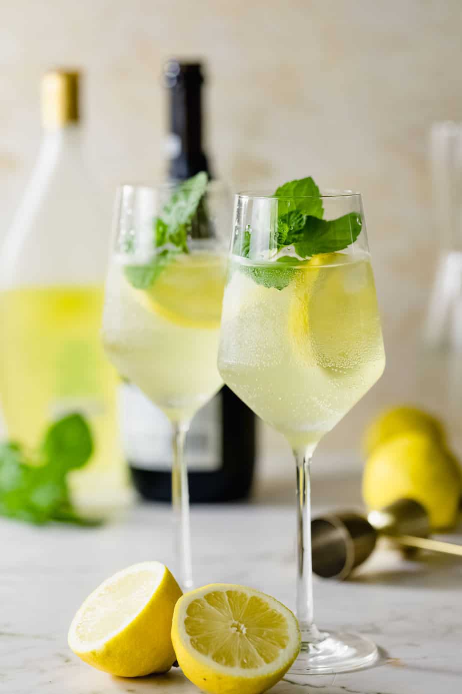Two limoncello spritz cocktails served in wine glasses sitting on a marble counter.