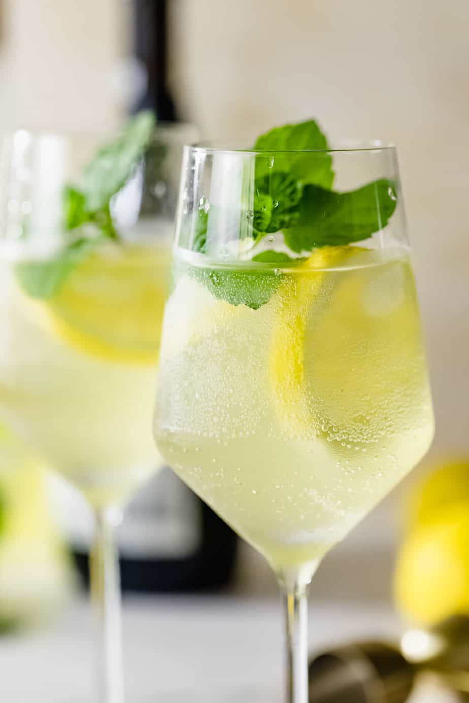 A limoncello spritz served in a wine glass and garnished with fresh mint leaves and a lemon slice.