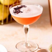 An Aperol gin cocktail topped with dried flowers sitting on a pink table.