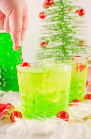 A bright green Grinch cocktail garnished with maraschino cherries.