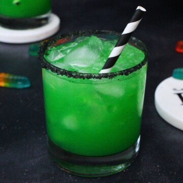 A green Beetlejuice cocktail served in a rocks glass with a black rim.