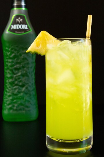 A bright yellow green June Bug cocktail served in a collins glass.