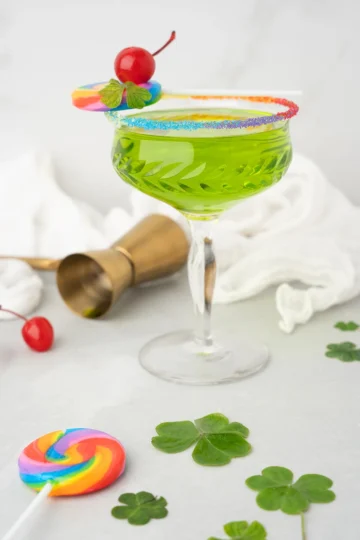 A liquid luck cocktail served in a coupe glass with a rainbow sugar rim.