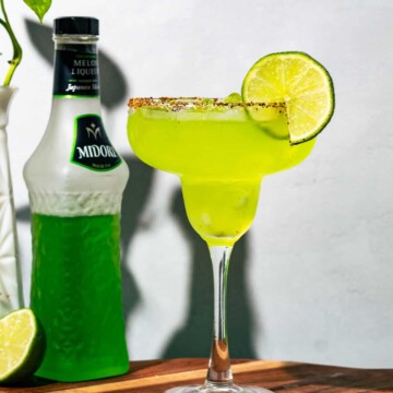 A bright green Midori margarita sitting next to a bottle of melo liqueur.