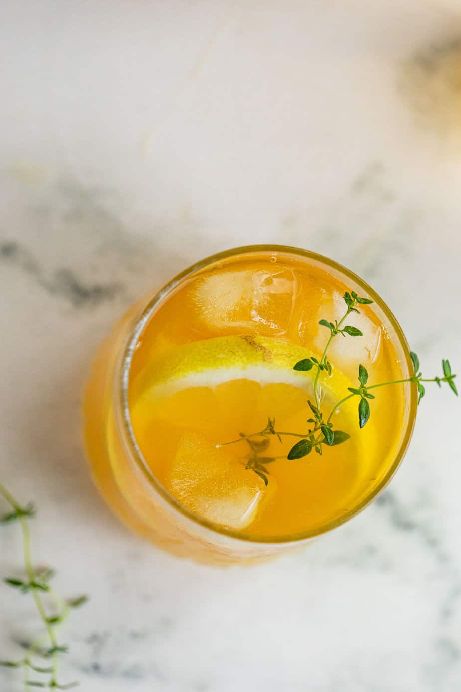 A rocks glass filled with whiskey and orange juice and garnished with a sprig of fresh thyme.