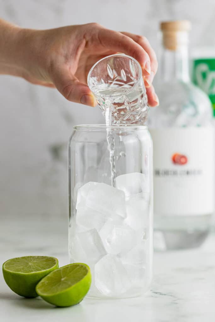 Gin being poured over ice in a highball glass.