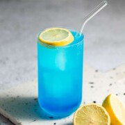 A Collins glass filled with an aqua velva cocktail garnished with a slice of lemon.