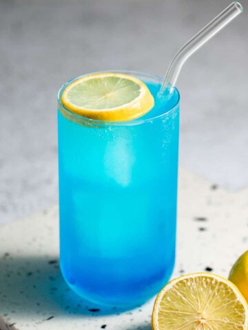 A Collins glass filled with an aqua velva cocktail garnished with a slice of lemon.