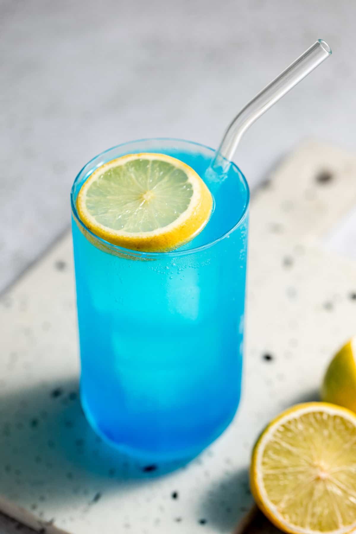 blue drink in tall glass with lemon slice as garnish and glass straw