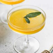 A bee's knees cocktail served in a coupe glass sitting on a counter.