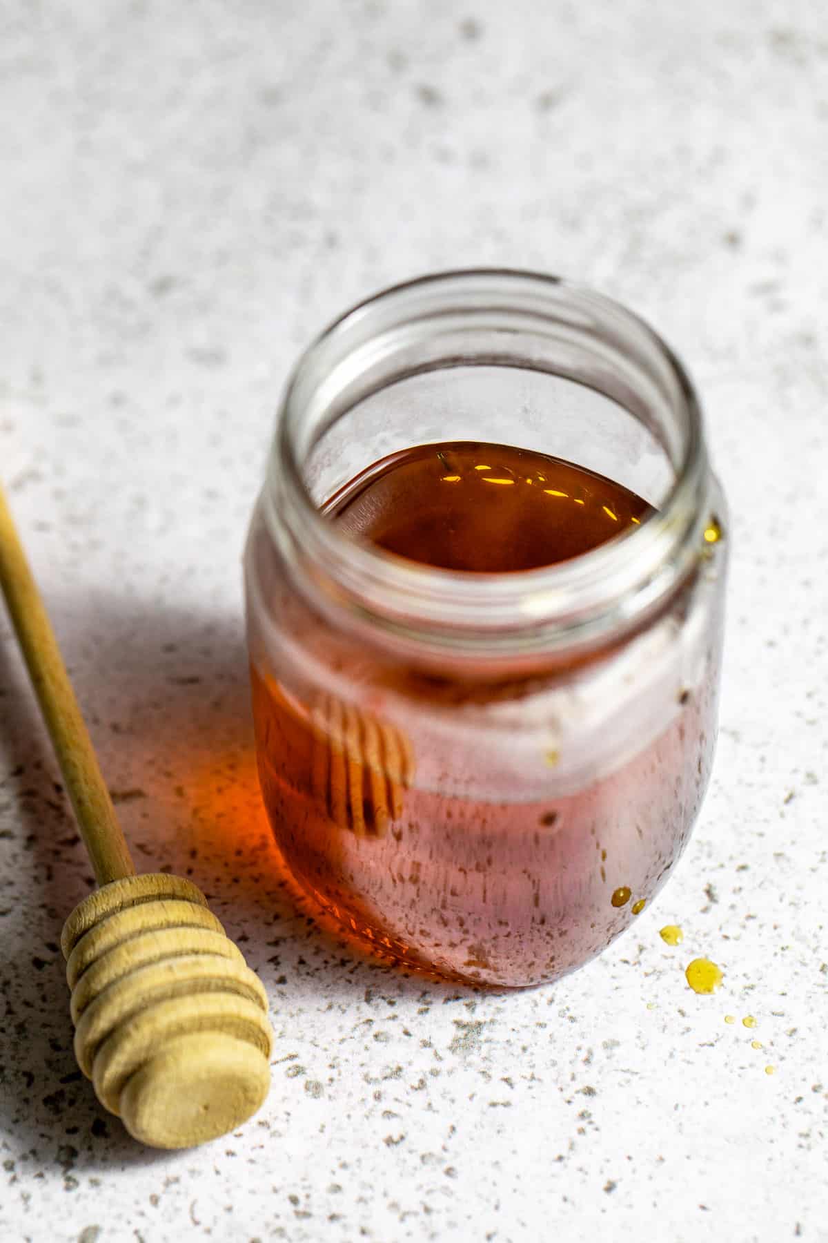 A mason jar filled with honey simple syrup sitting next to a honey dipper.