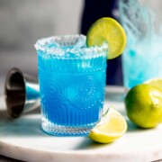 A blue margarita garnished with lime wedge sitting on a marble tray.