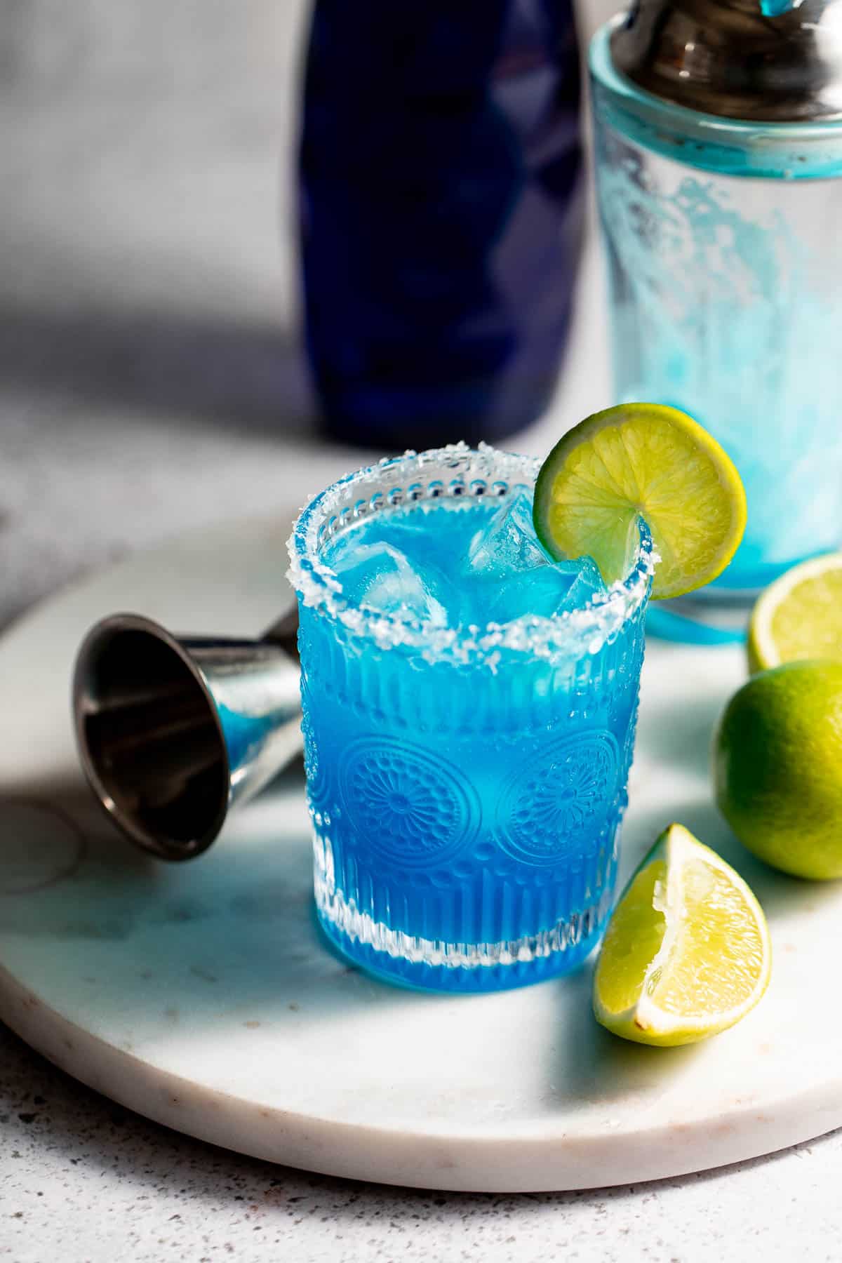 A blue margarita served with a lime wheel sitting on a marble tray.