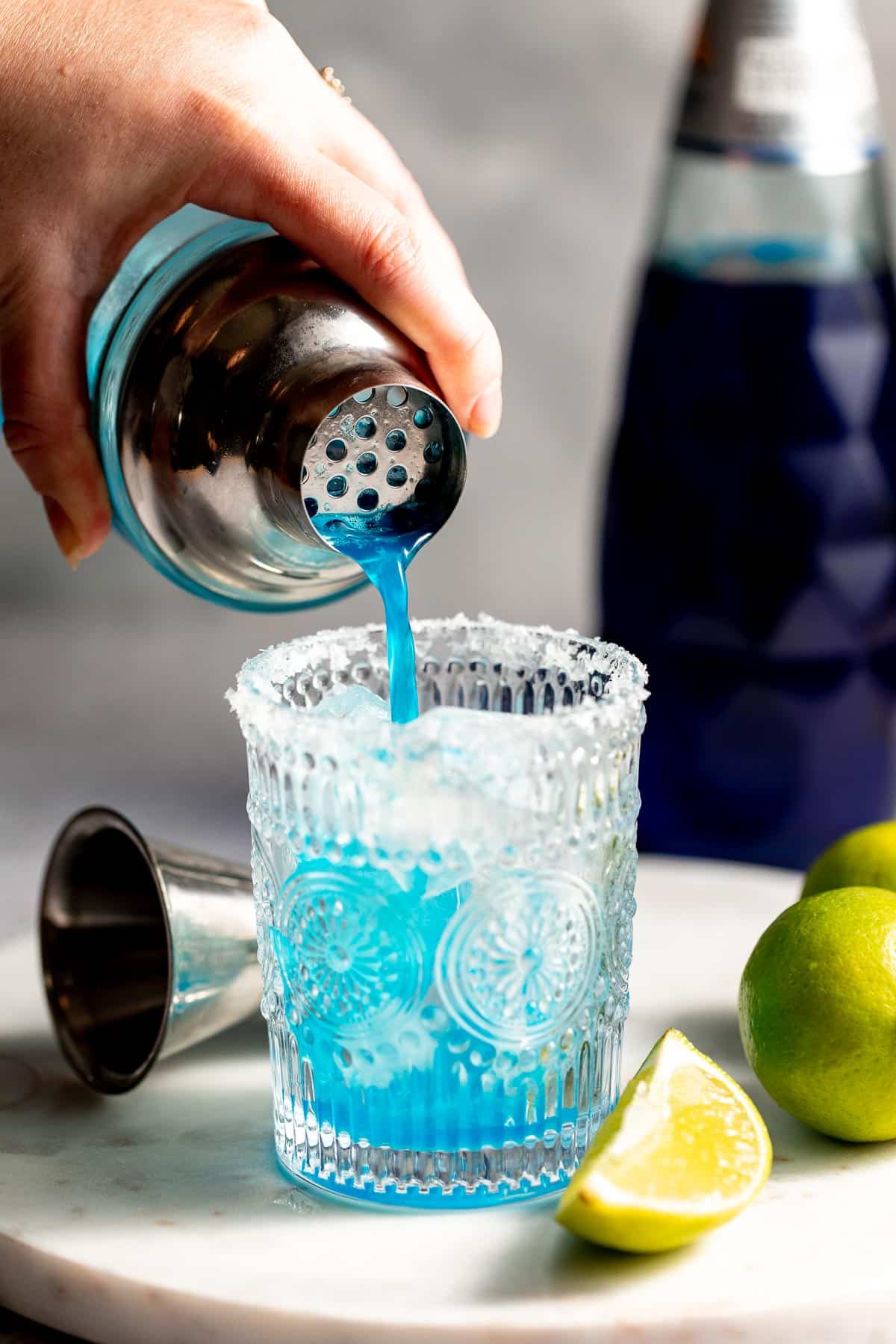 A freshly shaken blue margarita being poured from a cocktail shaker.