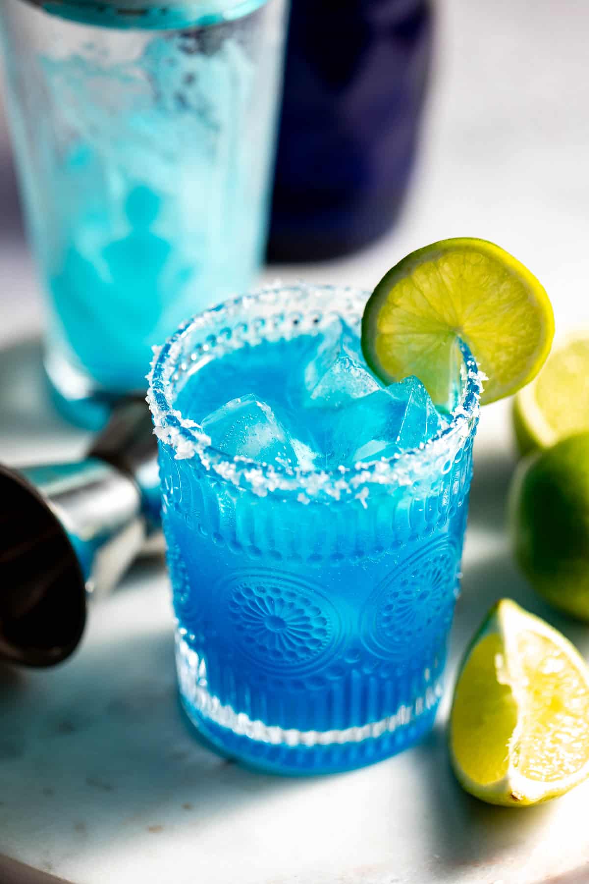 Blue margarita served in a rocks glass with a salted rim and lime wedge.