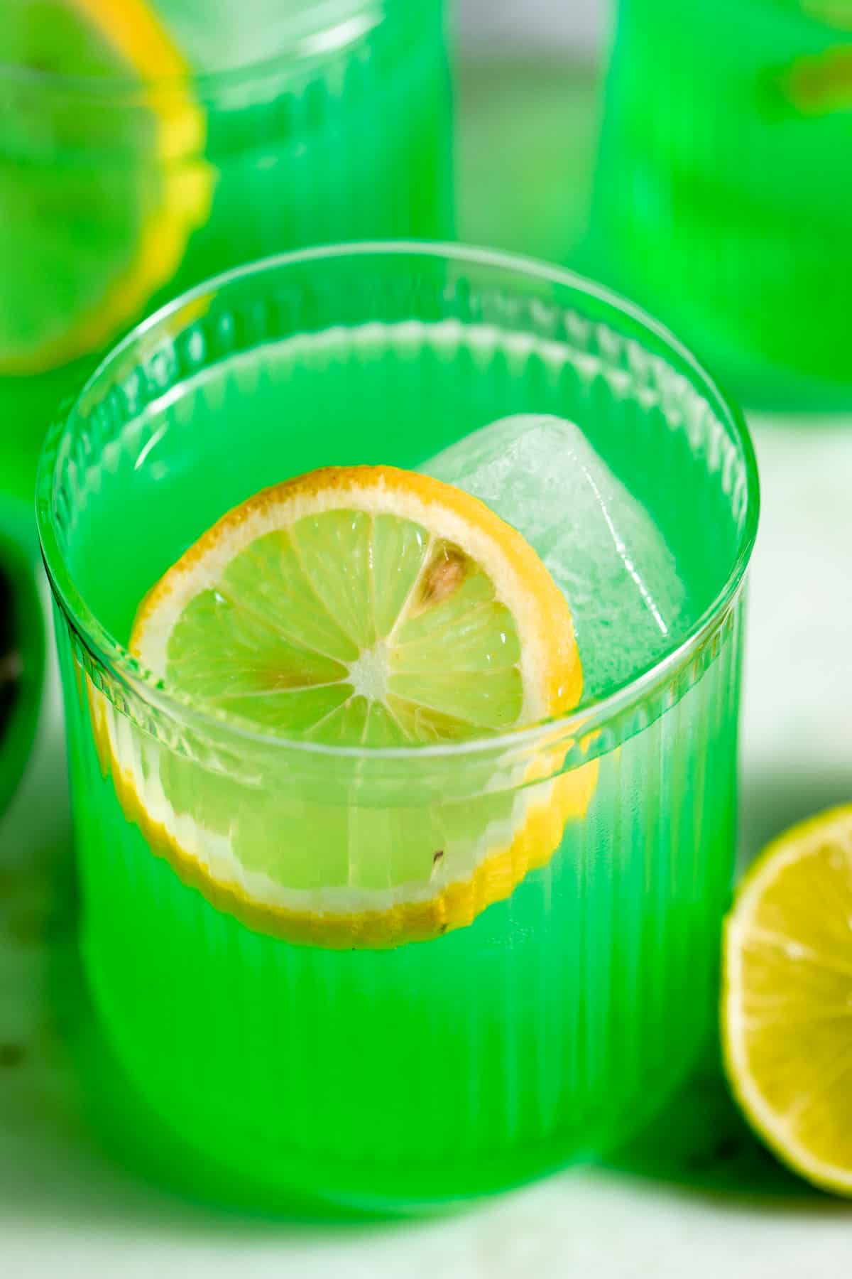 A glass of Midori sour garnished with a slice of lemon.