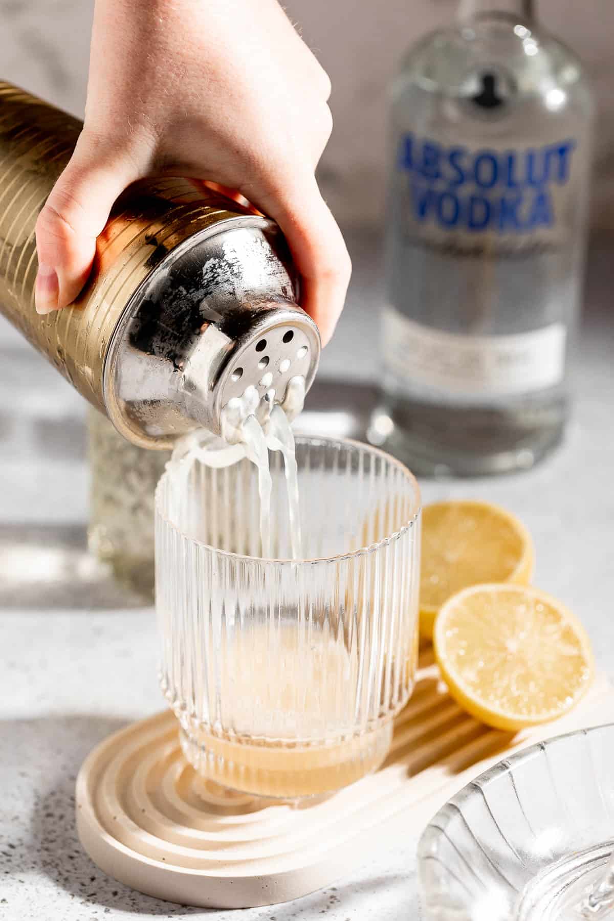 A vodka sour cocktail being poured from a cocktail shaker into a serving glass.