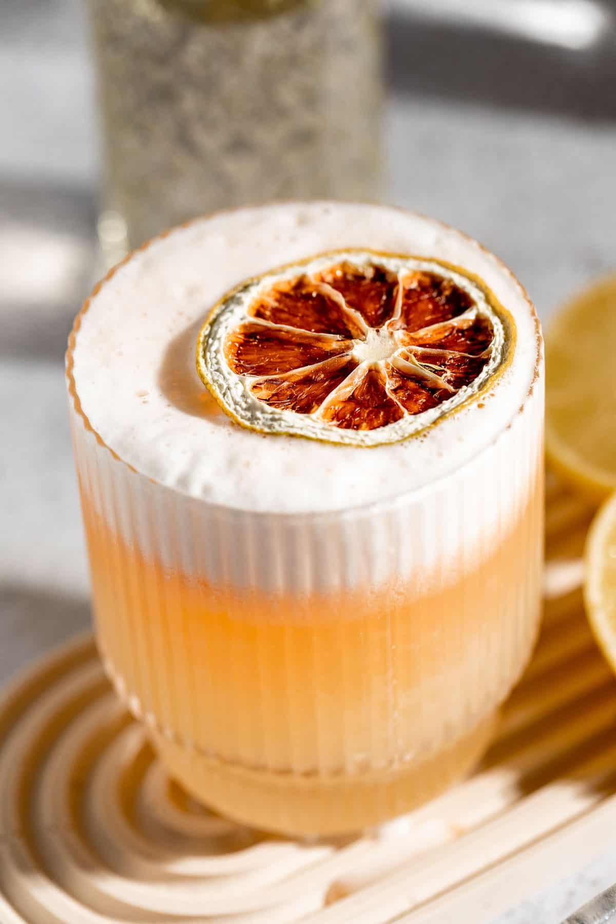A vodka sour cocktail garnished with a dried lemon slice.