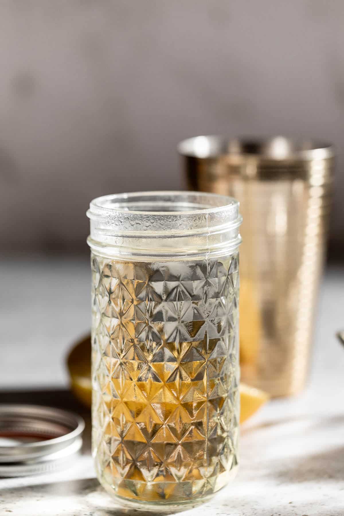 Simple syrup in glass jar with cocktail shaker in the background.