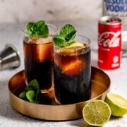 Two glasses of vodka and coke sitting on a gold tray.