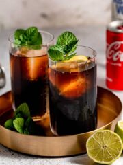 Two glasses of vodka and coke sitting on a gold tray.