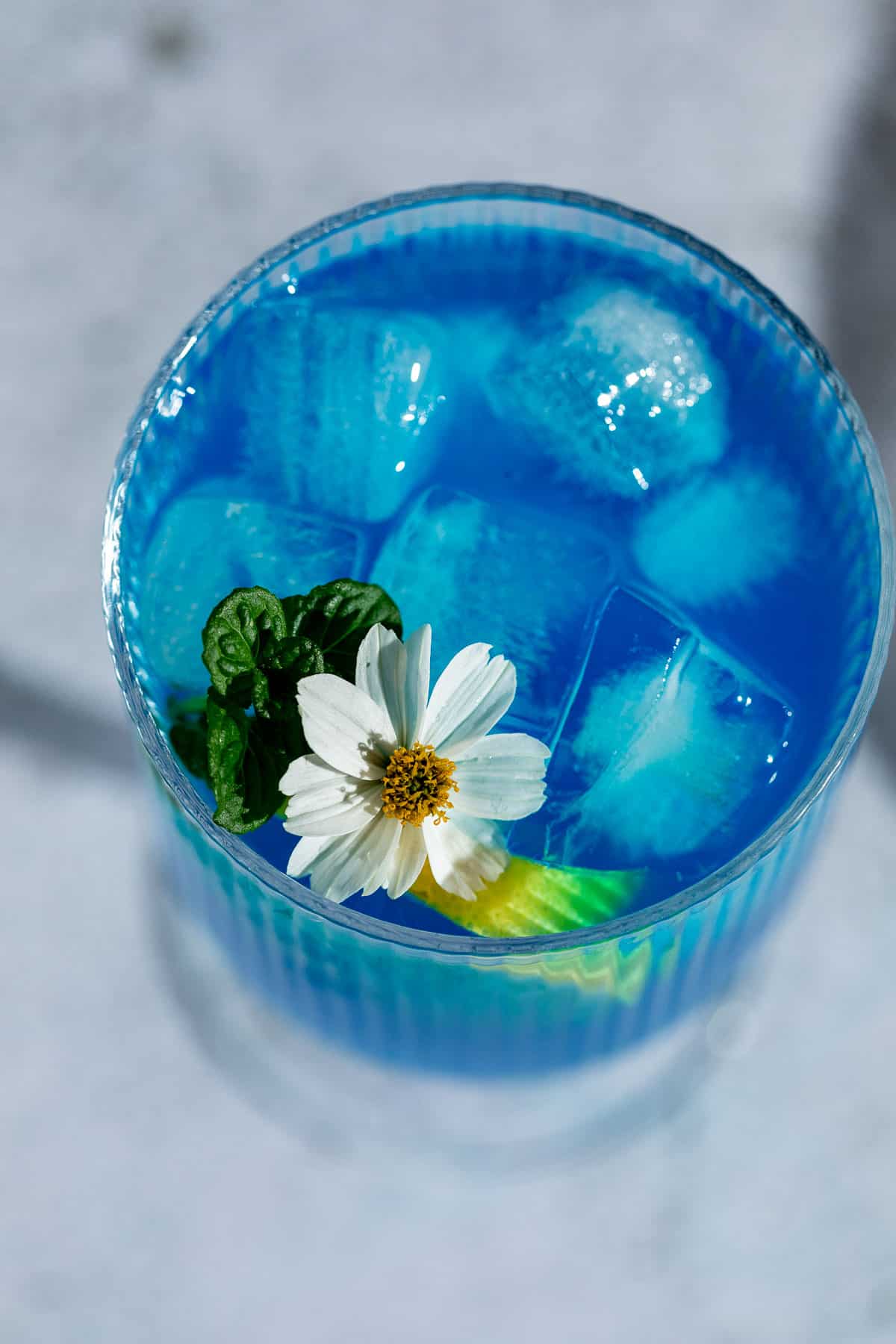 A blue motorcycle drink garnished with fresh flowers and a lemon slice. 
