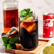 A tall glass filled with jack and coke sitting on a wooded tray.