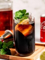 A tall glass filled with jack and coke sitting on a wooded tray.