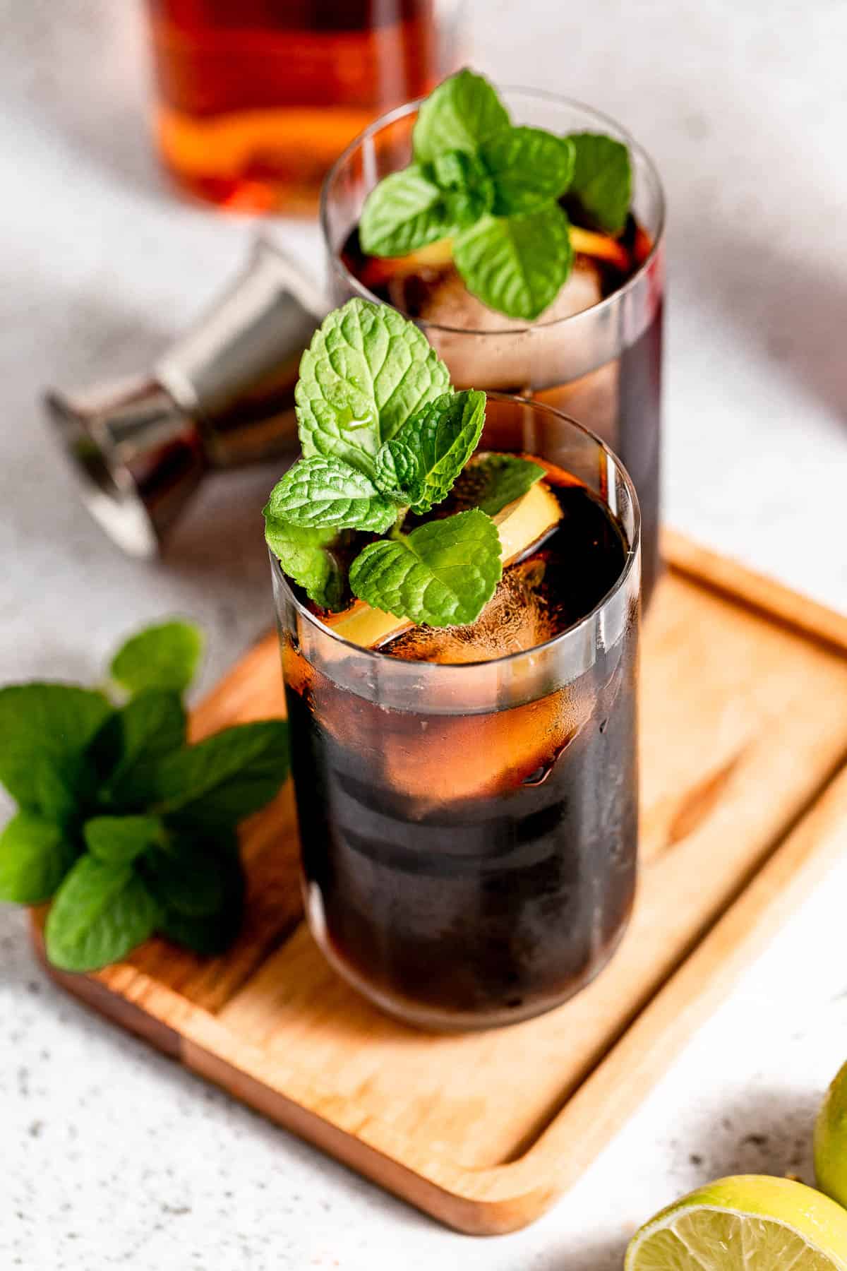 Two tall glasses filled with Jack and coke sitting on a small wooden tray.