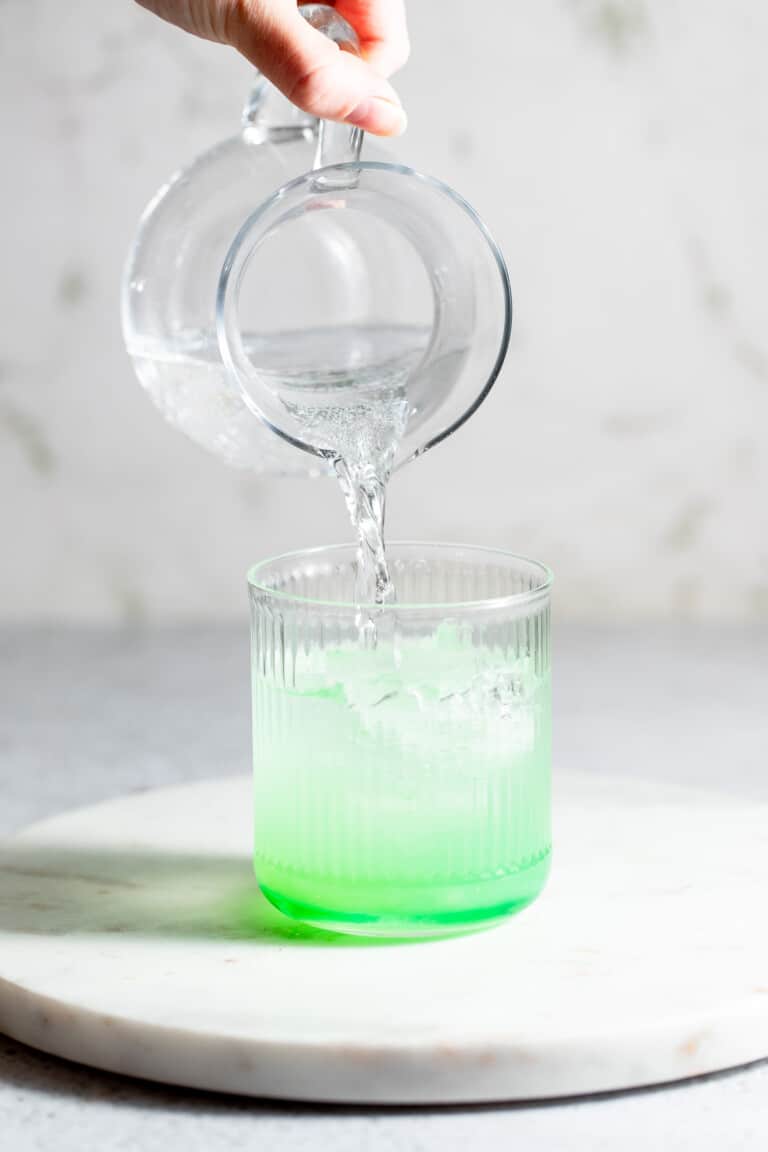 Soda water being poured into a glass to finish a Midori sour cocktial.