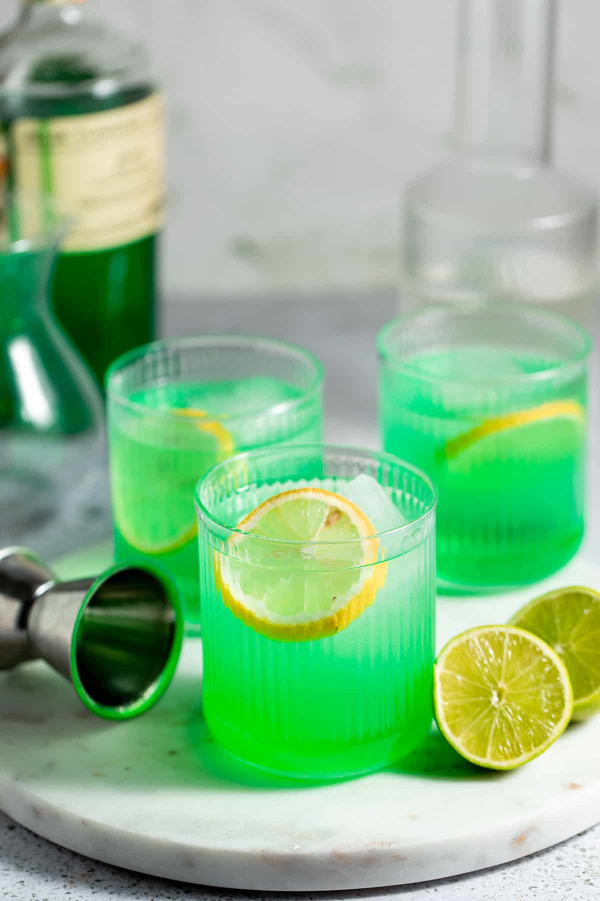 Three glasses of Midori sours sitting on a marble tray.