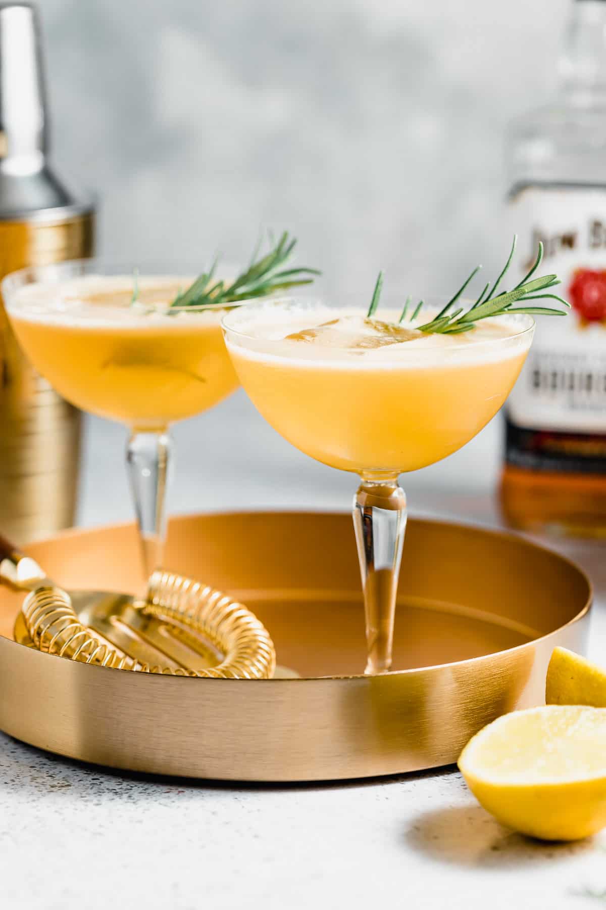 Two coupe glasses filled with bourbon smash and garnished with fresh rosemary.