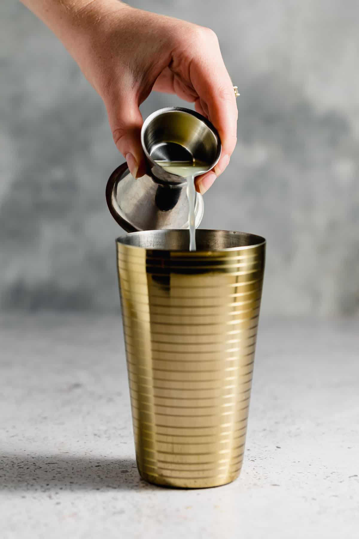 Lemon juice being poured from a jig into a gold shaker.