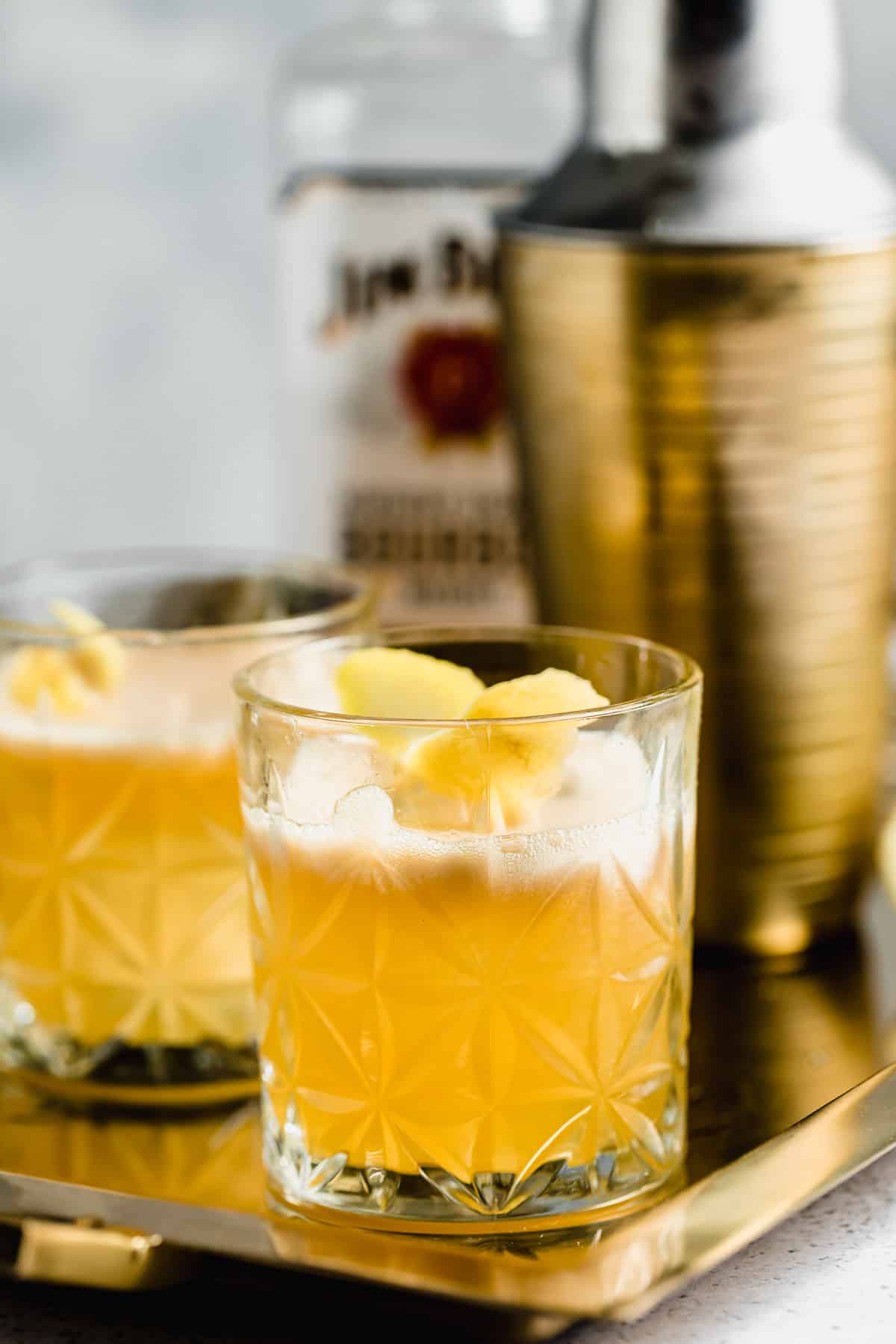 A gold rush cocktail served with a lemon twist on a gold tray.