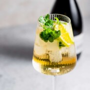 A Hugo Spritz cocktail served in a wine glass with fresh mint and lime wedges.