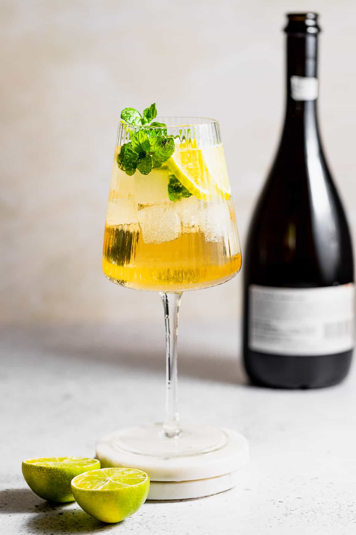 A wine glass filled with a Hugo Spritz cocktail sitting next to a bottle of Prosecco.