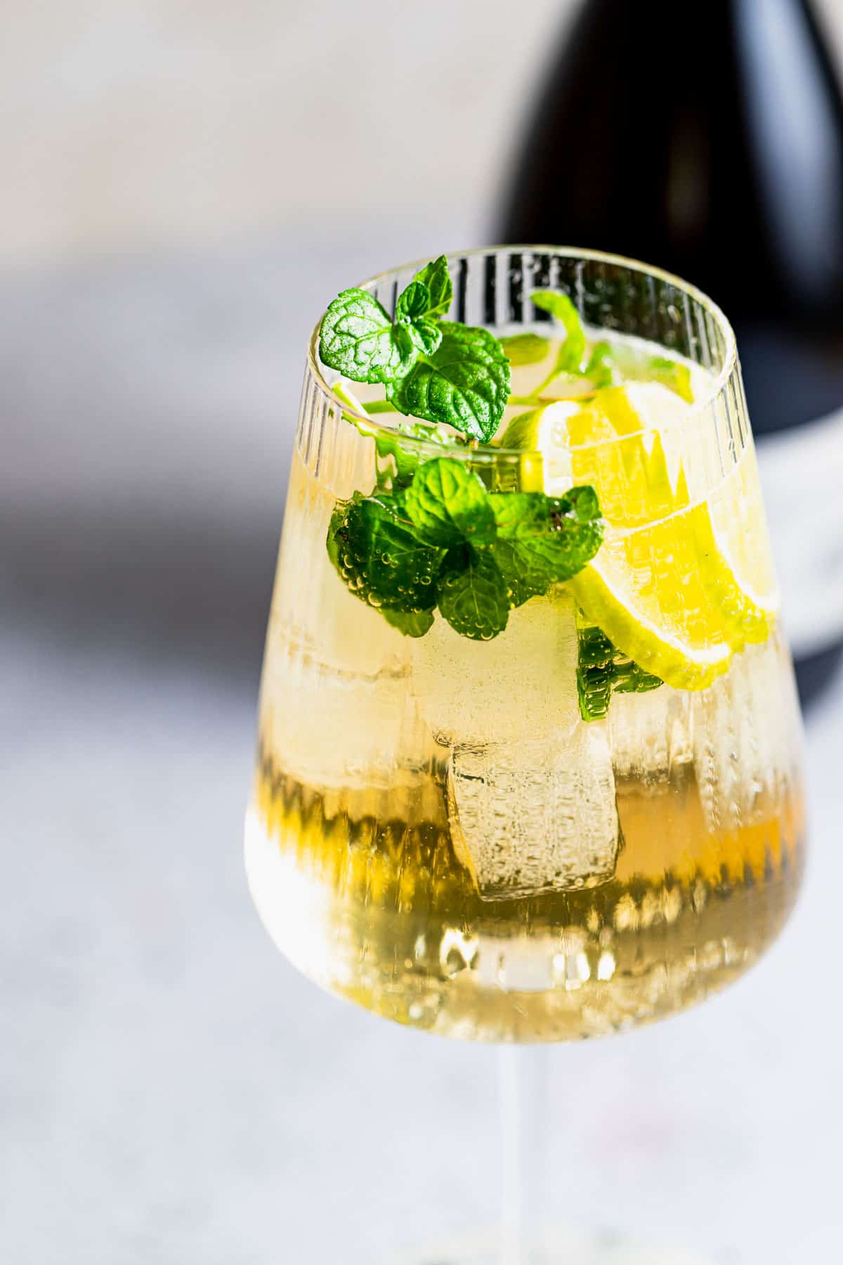 A Hugo Spritz cocktail served in a wine glass garnished with mint leaves and lemon.