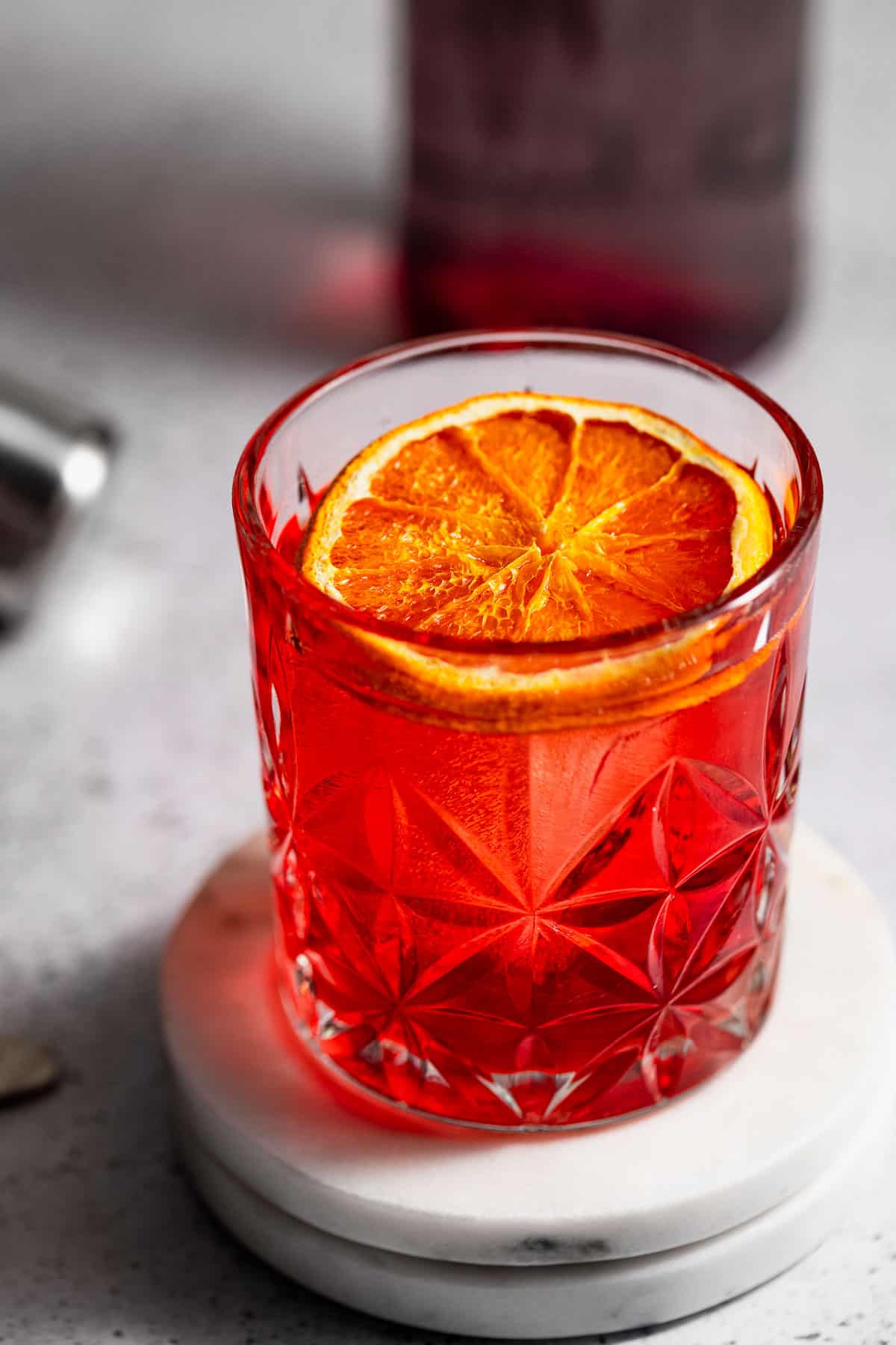 A mezcal negroni served with a slice of dried orange sitting on a countertop.