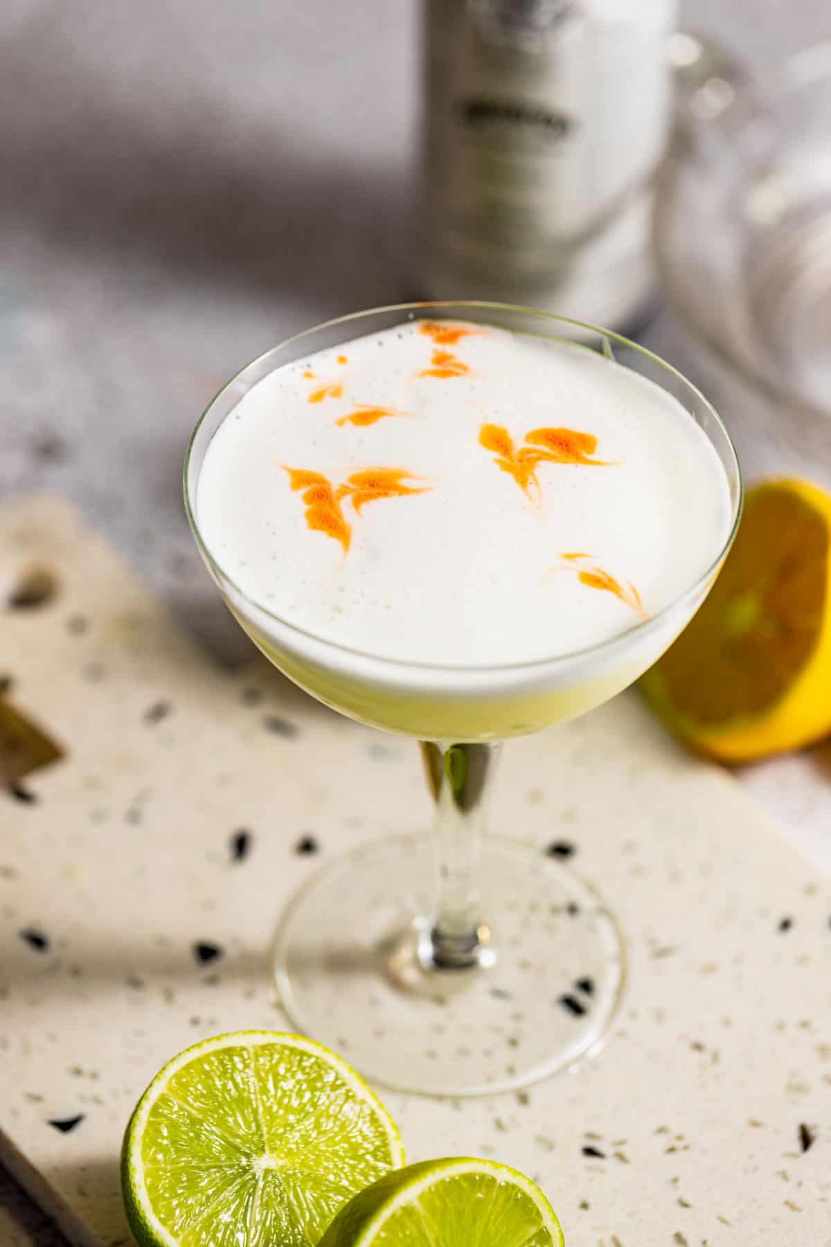 A mezcal sour served in a coupe glass sitting on a marble tray.